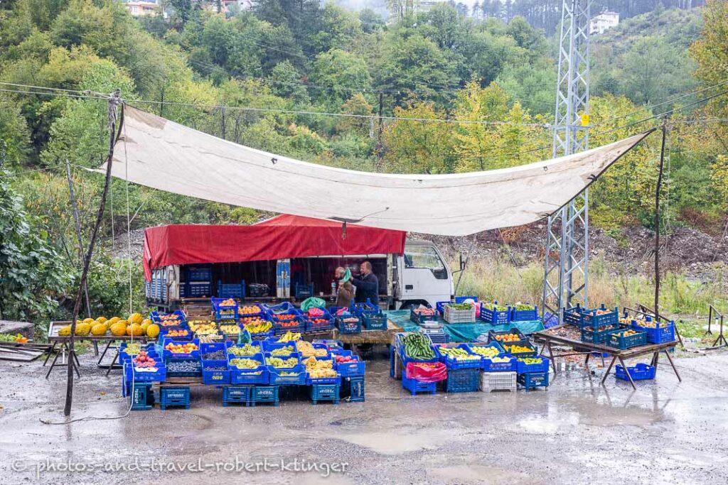 Two vendors selling fruits and vegetabels underneath huge tarp in the rain