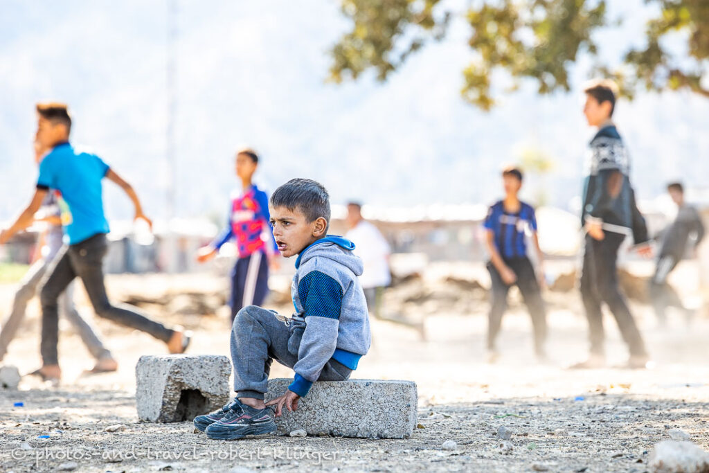 A boy sitting and watching other boys playing soccer in Iraq