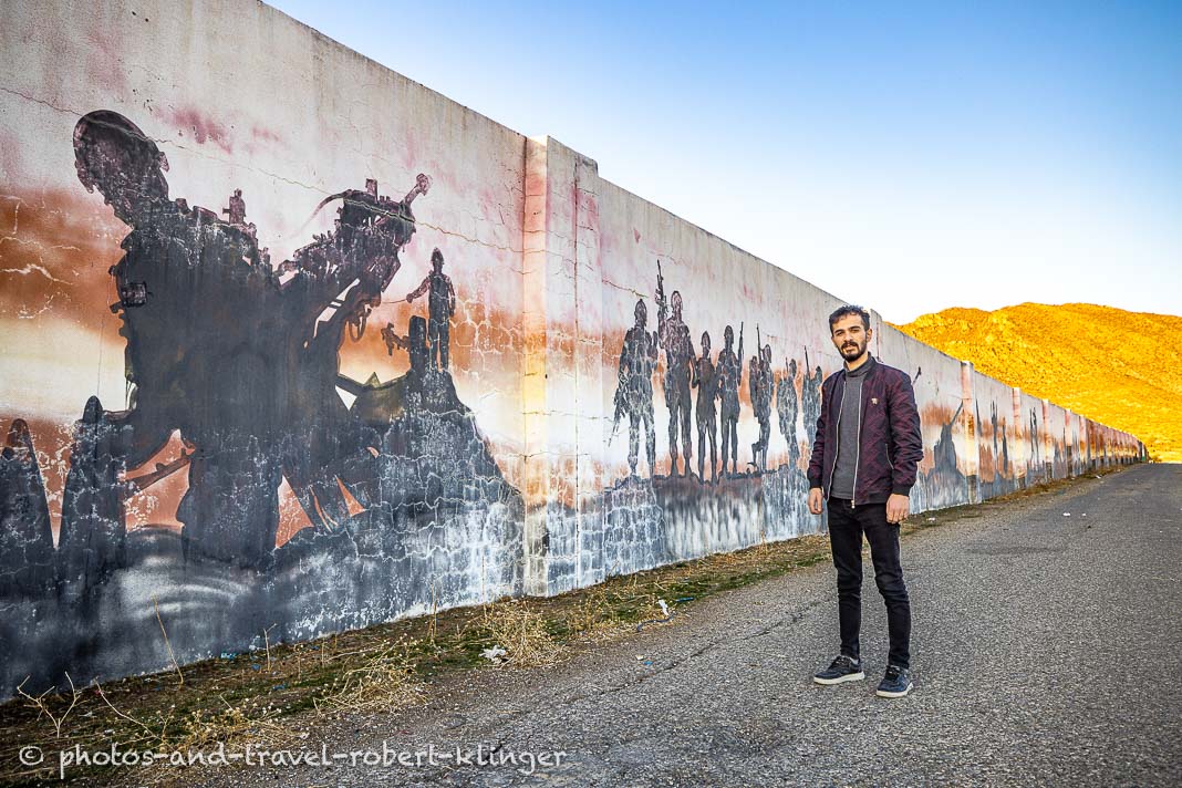A young man posing for a photo in front of a wall with military grafitis in Kurdistane, Iraq