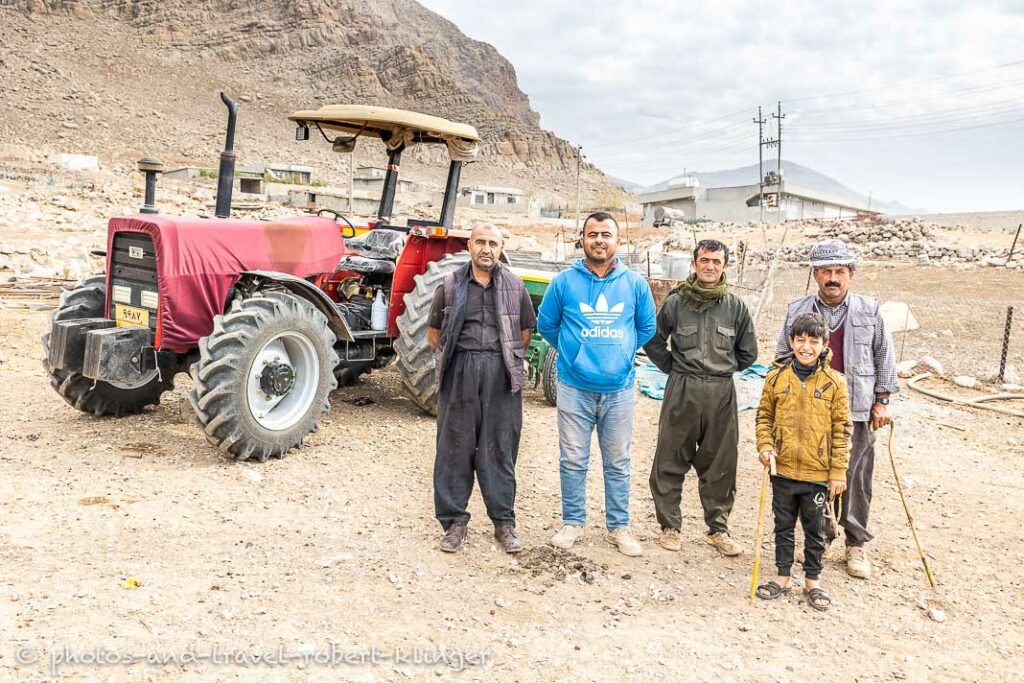 Four kurdish goat farmer and a boy are standing in a village in front of a tractor