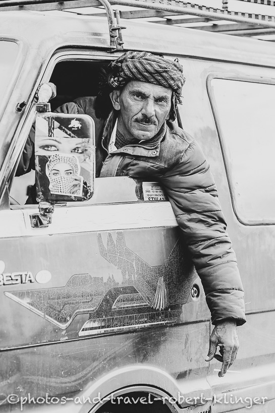 A kurdish man looking out of the window of his old van