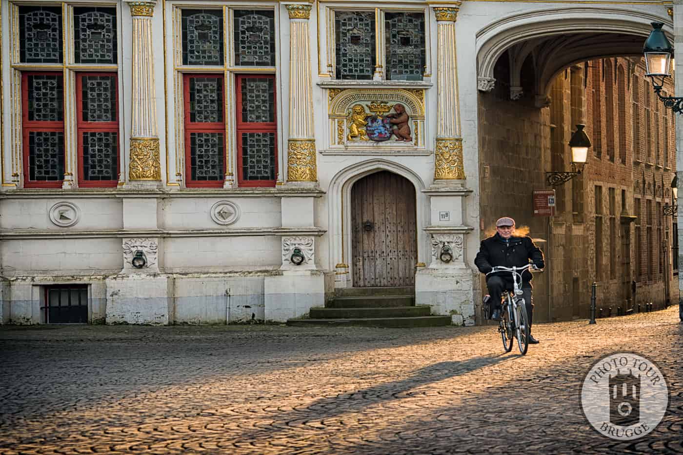 A lone biccle rider passes the city archive on the Burg square in Bruges Belgium. Photo by Photo Tour Brugge.