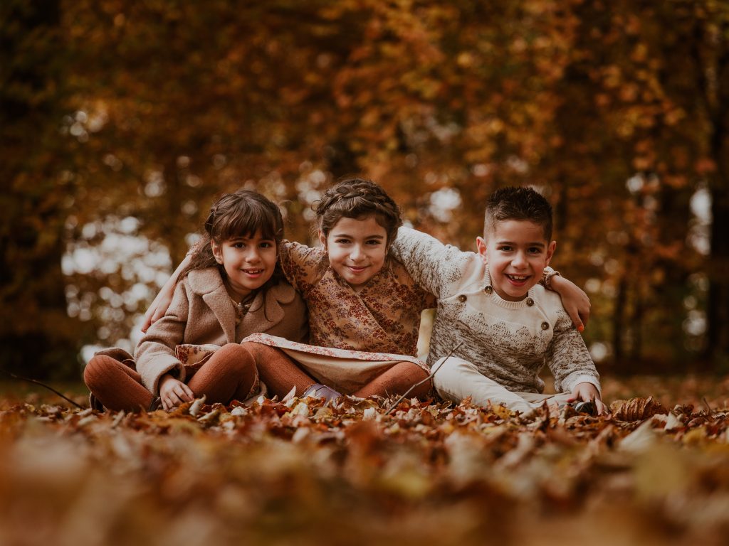 2 piger og en dreng sidder i efterårsbladene