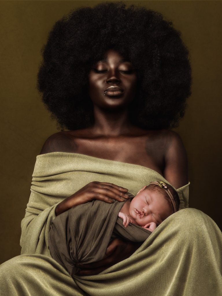 mørk kvinde med stor afro sidder i et grønt klæde med sin nyfødte pige der er wrappet i grønt wrap