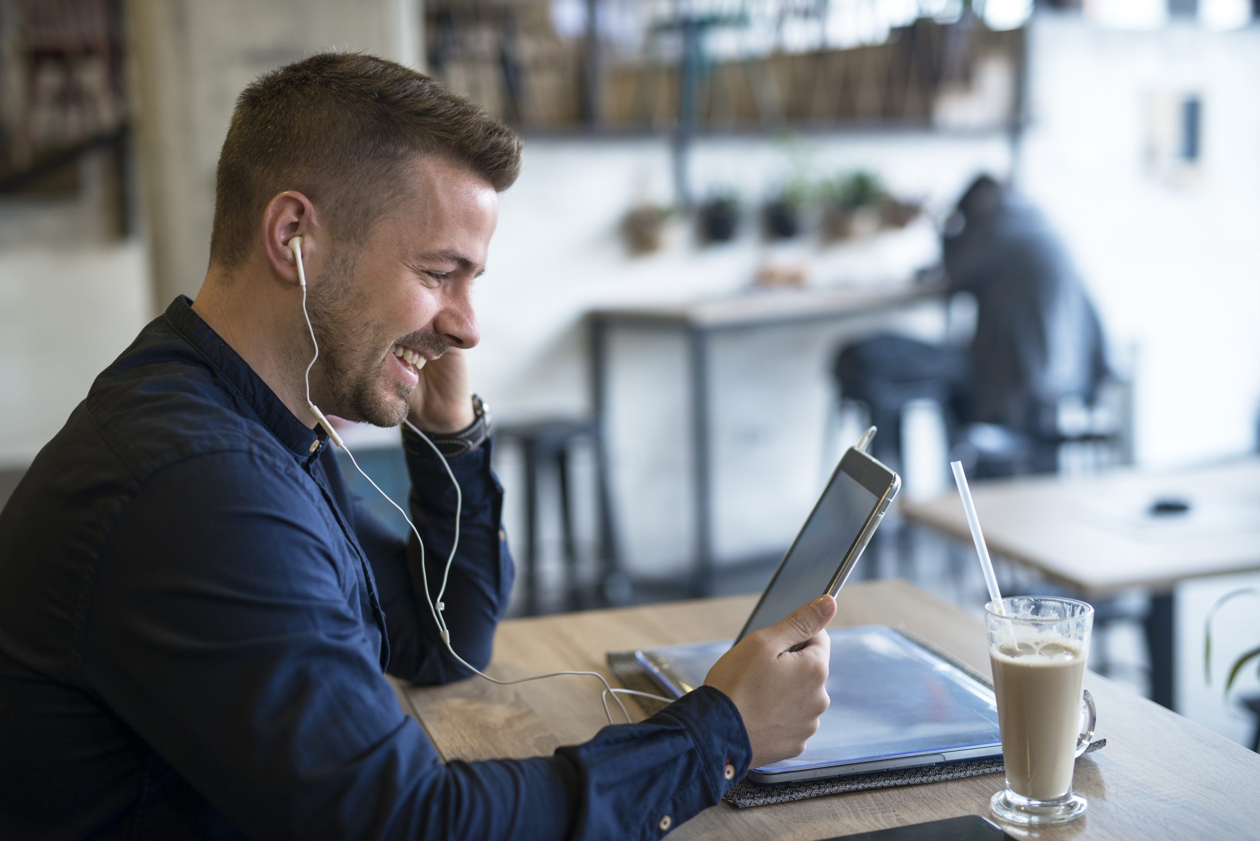 Successful businessman with headphones using tablet in cafe bar.