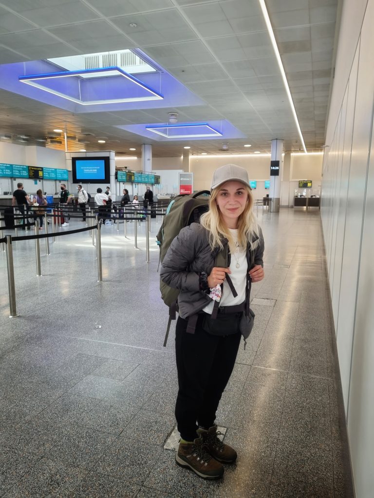 Amy is ready to go off backpacking for the first time. She is equipped with her rucksack that looks like it could be bigger than her at London Gatwick ready to check in for her flight.