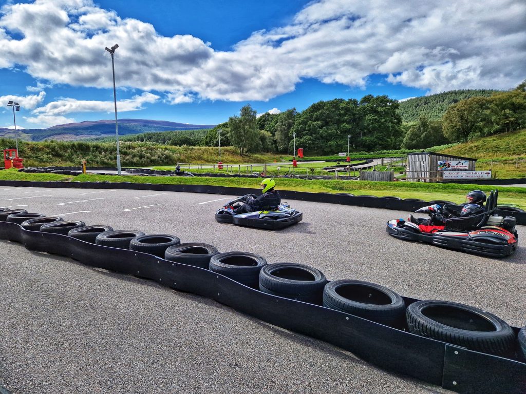 Go Karting is one of the cheap things to do in Aviemore on our list and this photo shows 2 of our friends go Karting in this stunning location with mountains in the background.