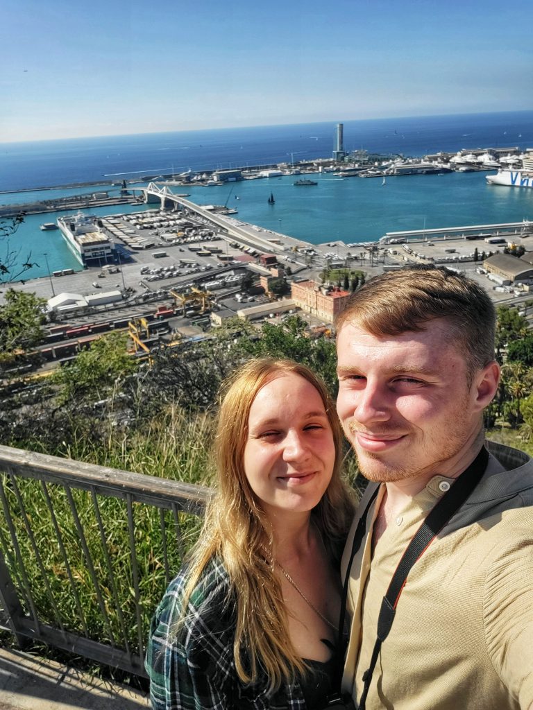 Amy & Liam taking a photo together with a beautiful marina viewpoint behind them.