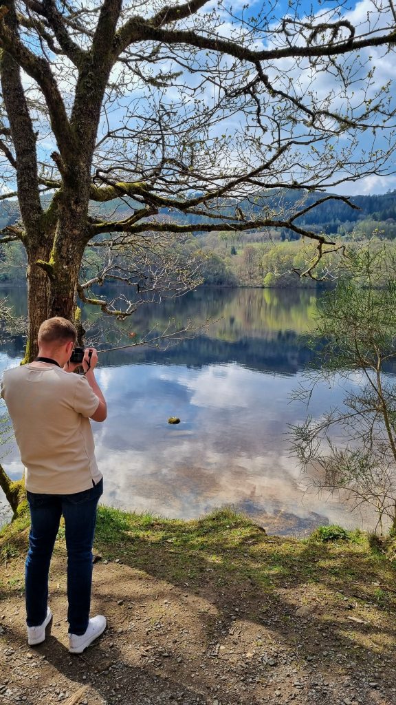 Liam using our Canon EOS M50 Mirroiless camera to take some photos of the loch in Pitlochery