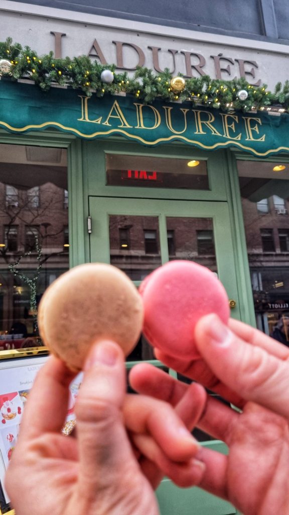 2 of the Macaroons that we tried at Laduree. The photo shows a salted caramel and rose flavoured macaroon held up in front of the Laduree shop front.