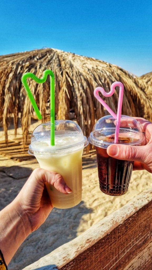 Cocktails that we purchased at Paradise Island with the palm tree parasols in the background. Our cups with the cocktails also came with bendy straws that have been bent into the shape of hearts which looks super cute.