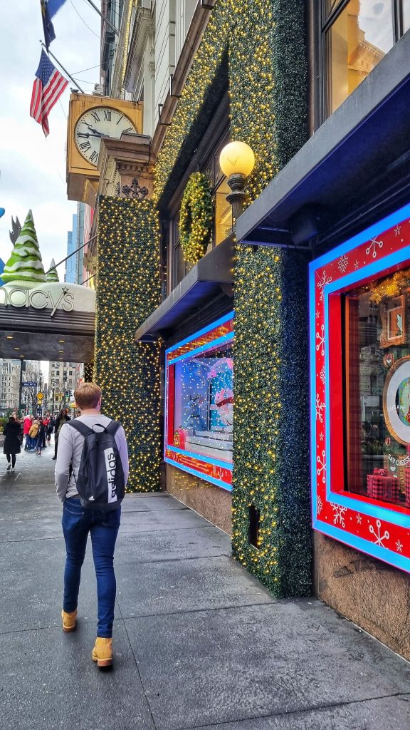 Liam walking past one of the shops in NYC that is decorated with plenty of lights and greenery for the festive season.