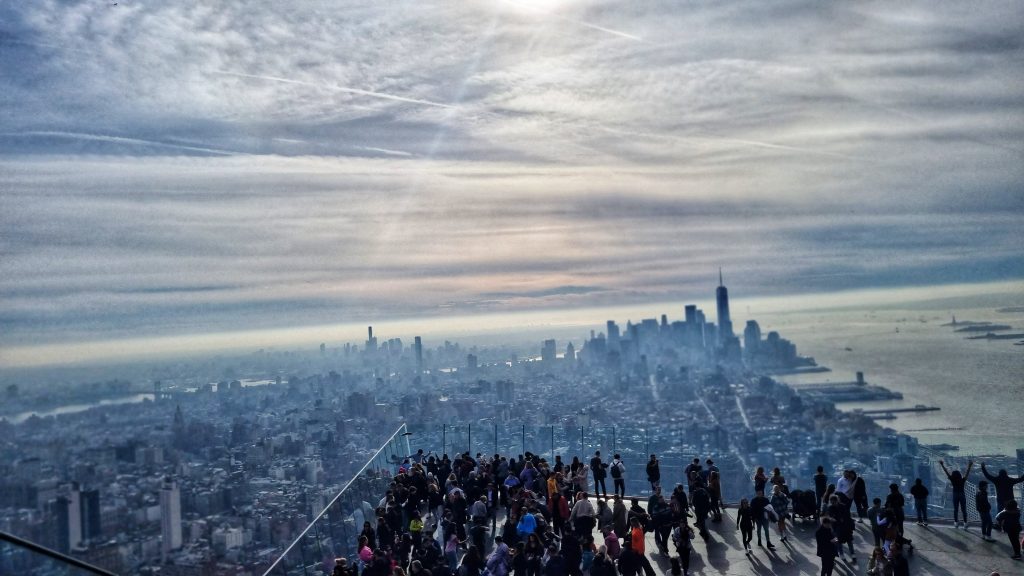 View of New York City skyline from The Edge with loads of people crowded by the glass to catch a glimpse of the view. If you're looking for things to do for couples in NYC you can also climb up the side of the building too