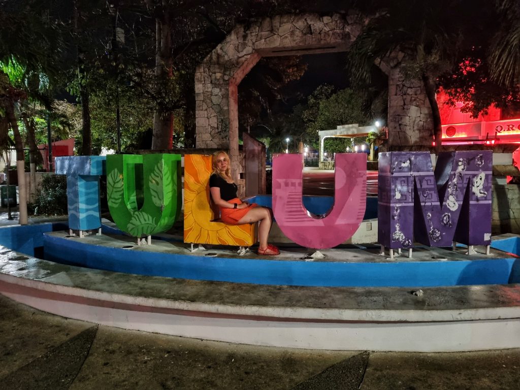 Multi-coloured Tulum sign with Amy sitting on the L shape.