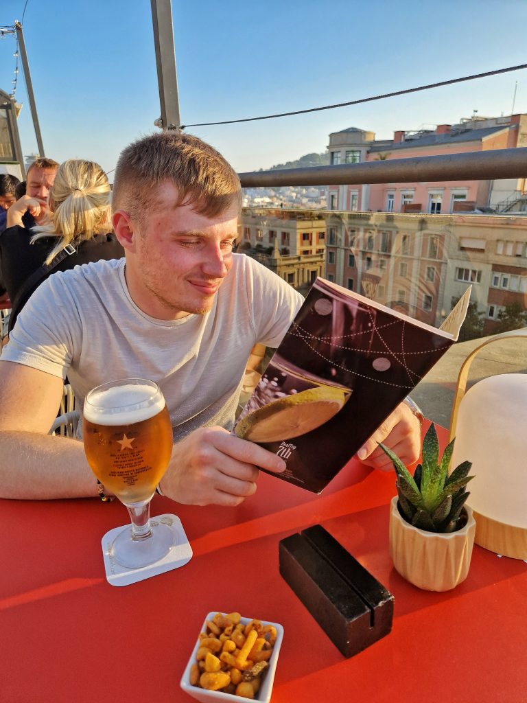 Liam choosing from the menu in one of the rooftop bars with a beer.