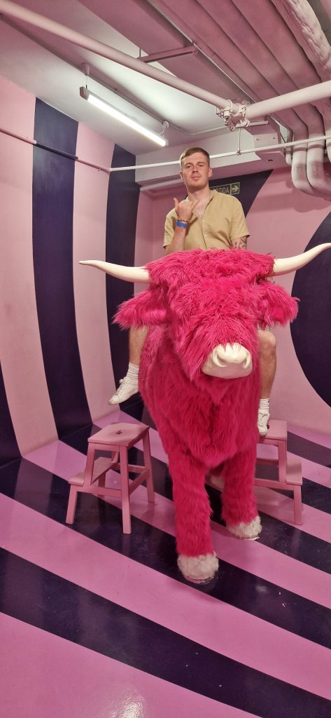 Liam posing on a pink highland cow at the Big Fun Museum. This is one of the most fun cheap things to do in Barcelona Spain.