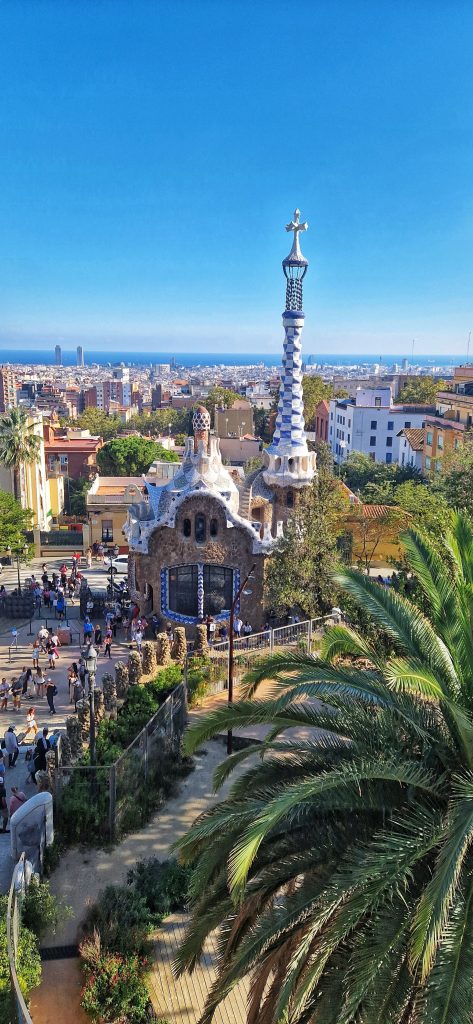 Parc Guell is not the cheapest thing to do but it is certainly one of the main tourist attractions in Barcelona. This image shows the buildings in Parc Guell and plenty of crowds too with Barcelona City in the backdrop.