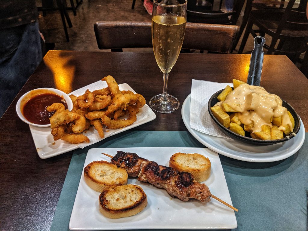 Some of the tapas options available in Barcelona including patatas bravas, pork skewer and chicken bites with a glass of prosecco.
