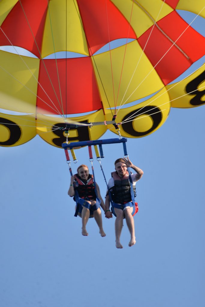 Amy & Liam holding hands whilst in the air parasailing.