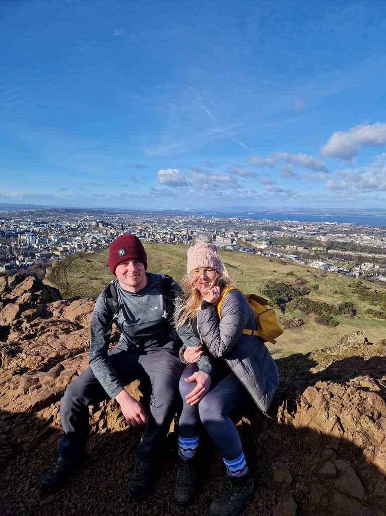 Amy & Liam at the top of Arthur's Seat with a view of Edinburgh city in the background.