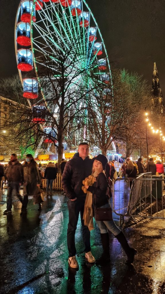Amy & Liam standing in front of the Ferris wheel for Edinburgh's Christmas Markets.