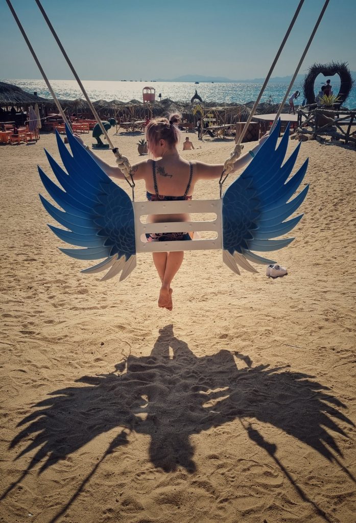 Amy sitting on a seat with wings at paradise island creating a shadow on the sand of her with wings