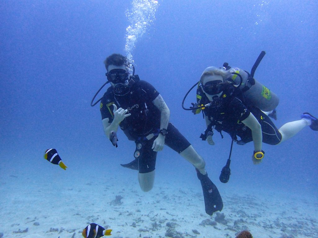 Amy & Liam scuba diving in Phuket with fish around them. We visited in October and this was the best time to visit Phuket for us as it was a quieter period due to the rainy season and the dive sites were beautiful