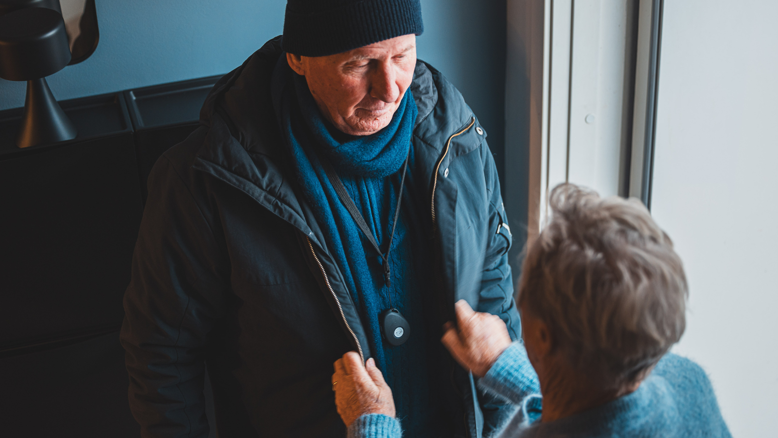 An older man with a jacket. An older woman is standing in front. 