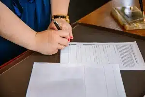 Osoba podpisująca dokumenty leżące na biurku.