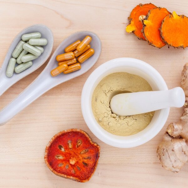 Kapseln, Naturprodukte wie Ingwer und ein Mörser mit Pulver in der Mitte