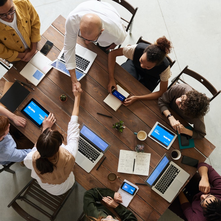 overhead wooden desk of people at laptops and shaking hands