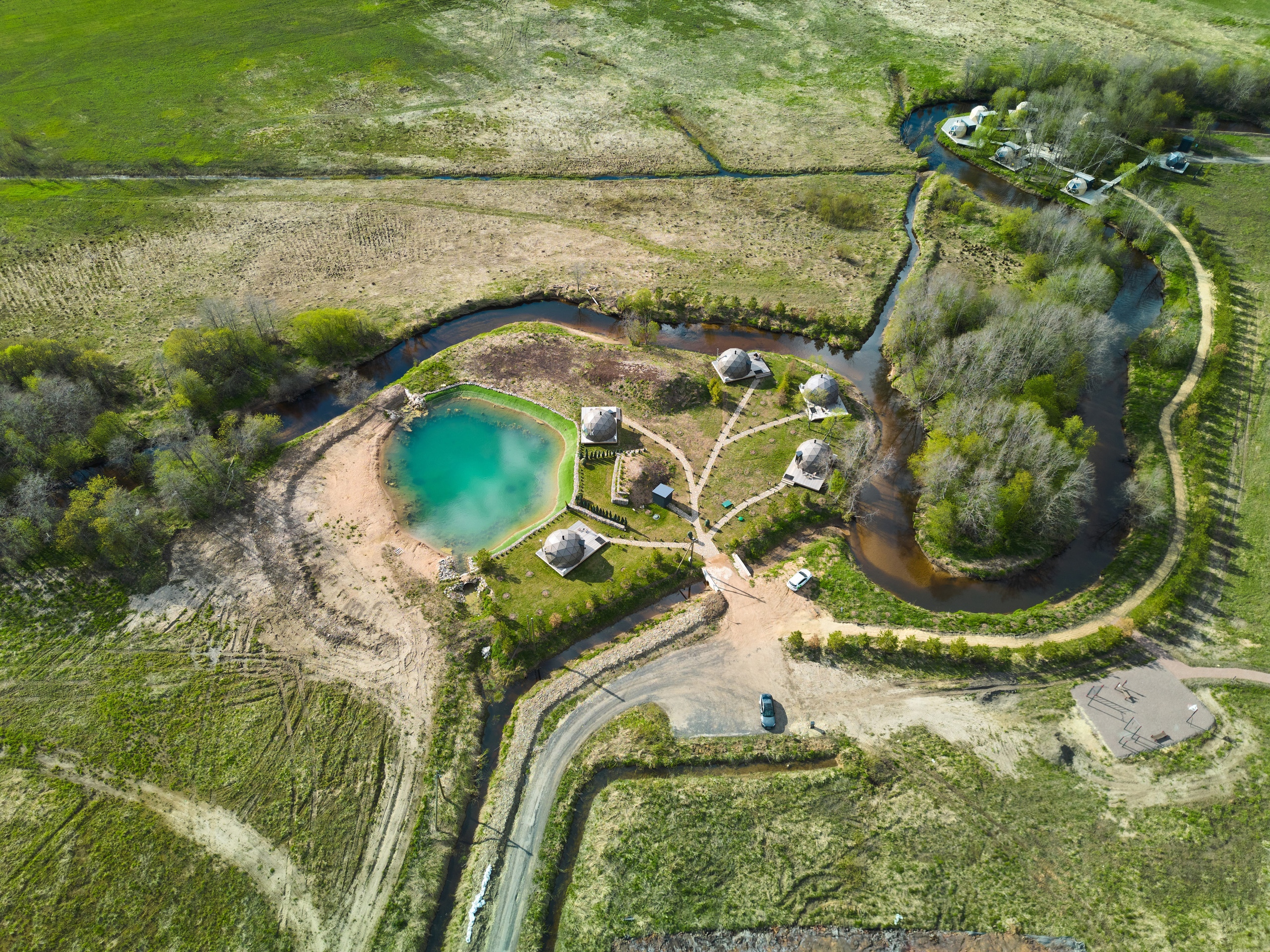 Experience a stunning aerial view of a rustic retreat with charming cabins and a peaceful healing pond