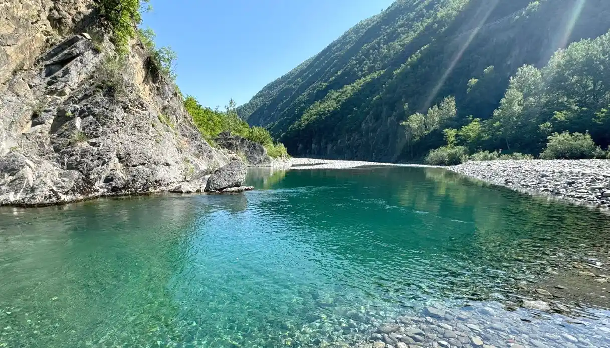 Una spiaggia di ciottoli bianchi e acqua limpida color turchese del fiume Trebbia, meta ideale per una gita fuori porta da Pavia durante l'estate.