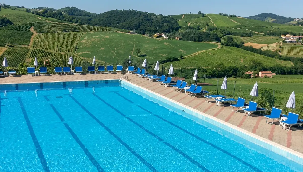 Quattro persone si tuffano in una piscina all'aperto nel pavese durante una giornata di sole estivo.