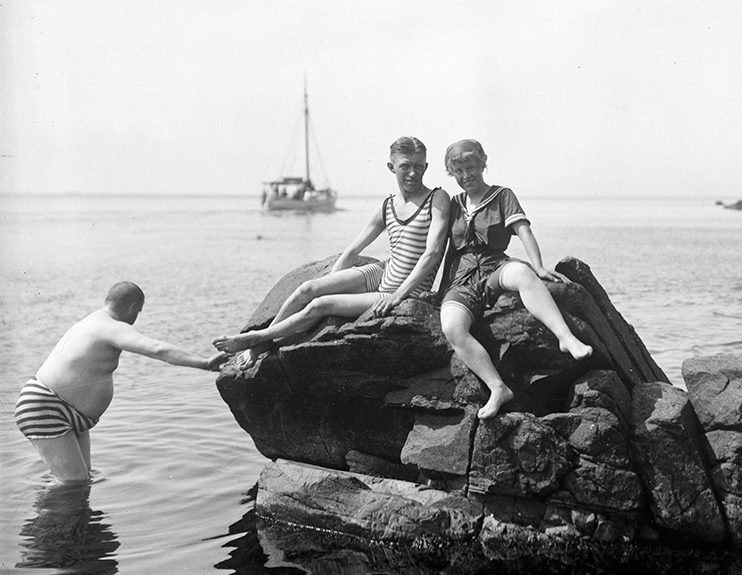 Män och kvinnor som sitter på klippor och badar i havet i mölle