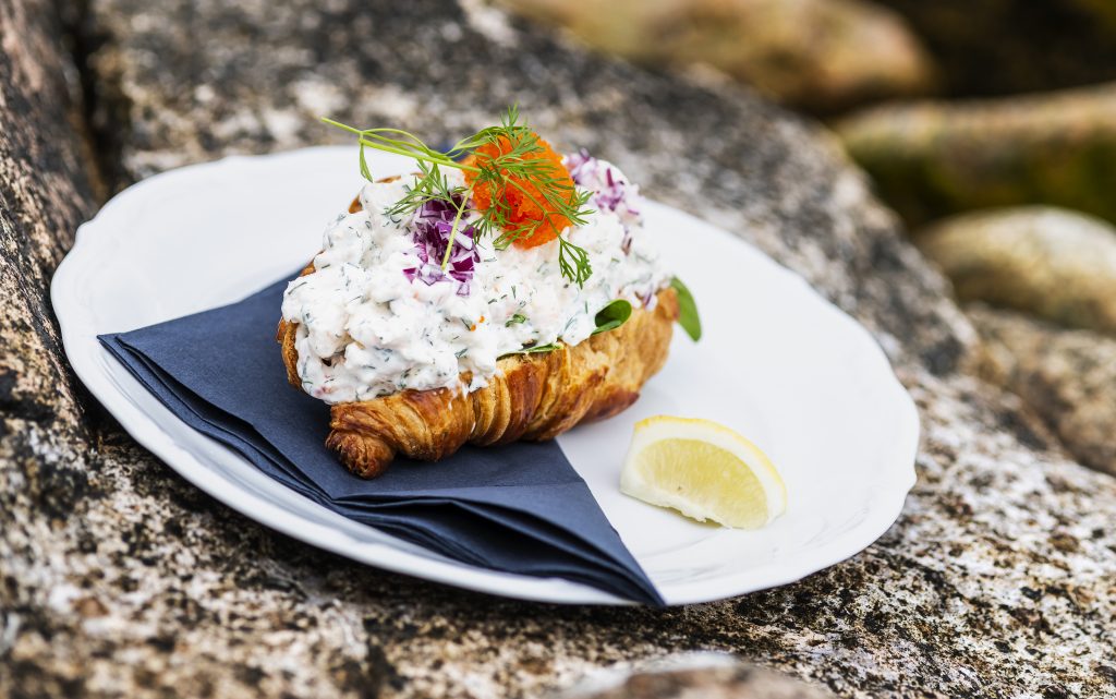 En croissant fylld med skagenröra på en tallrik på en sten