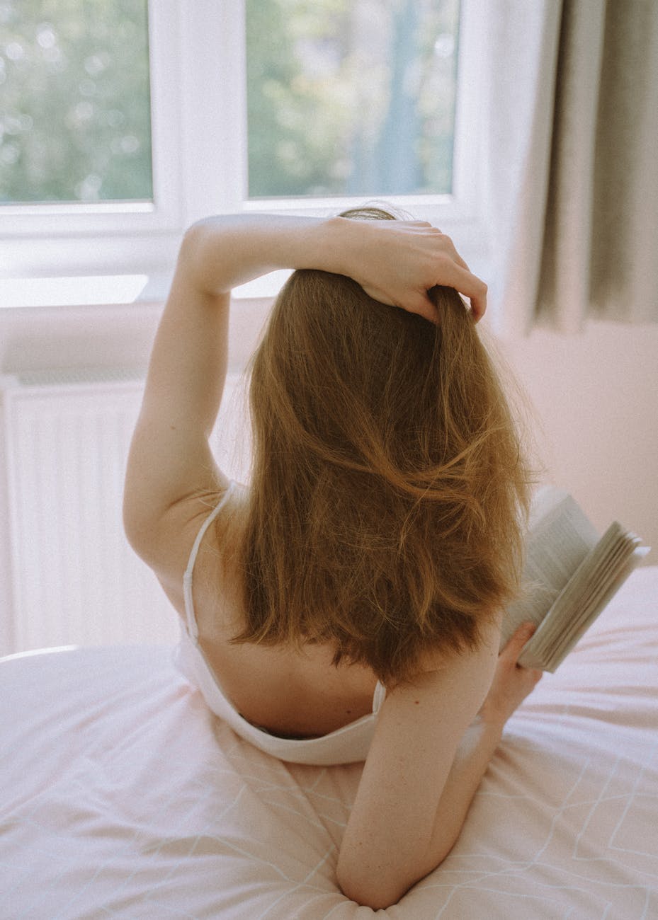 back view of a woman sitting on a bed while holding a book