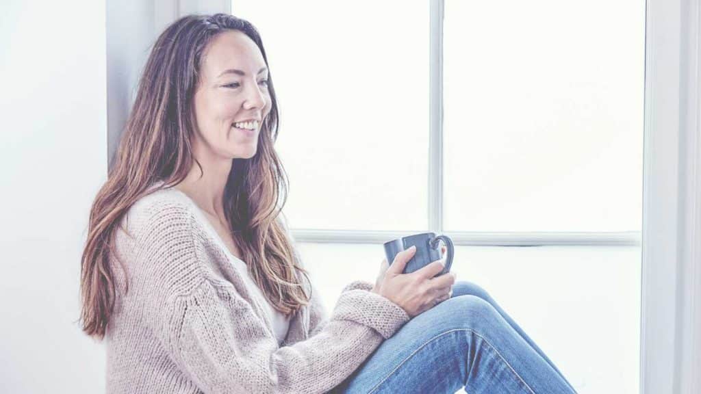 Billedet forestiller lifecoach Mia Korsgaard, som sidder i en vindueskarm med en kaffekop i hånden og smiler.