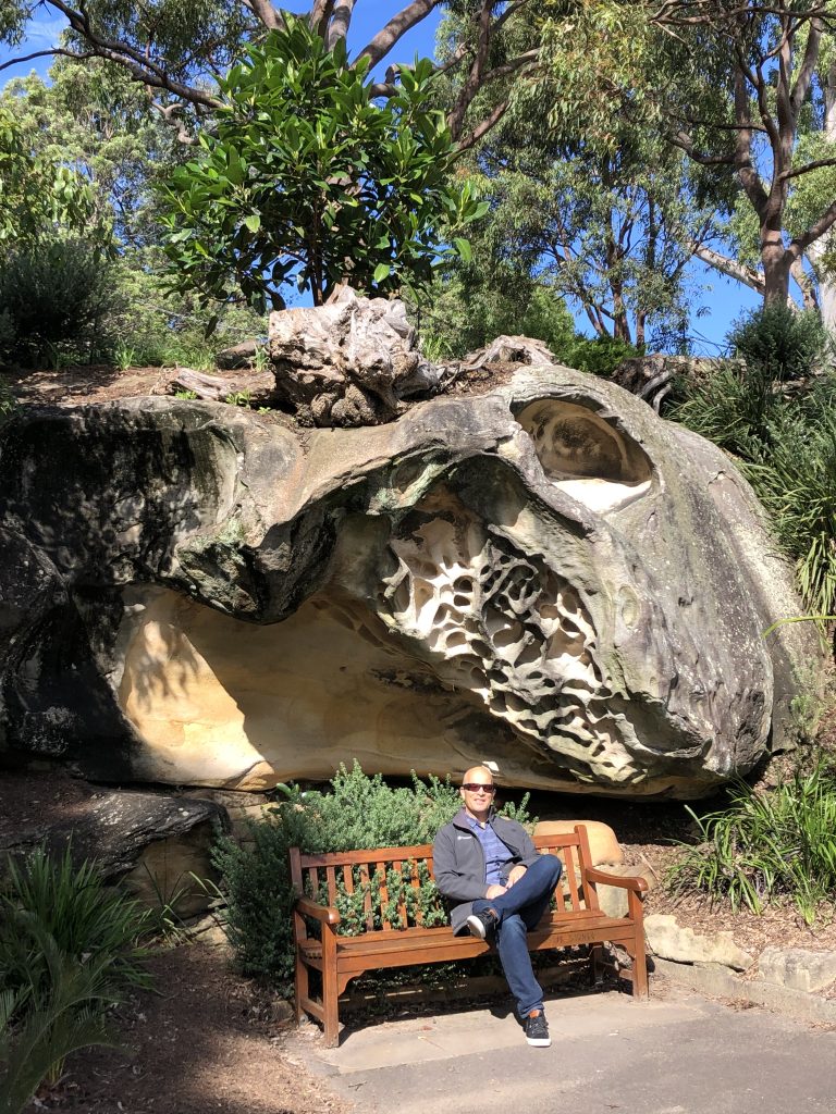 Allan in on a bench in front of a large rock in the Royal Botanic Garden