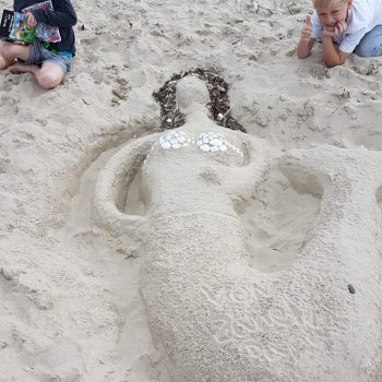 Zwei Jungs bauen eine Meerjungfrau am Ostsee-Strand aus Sand nach