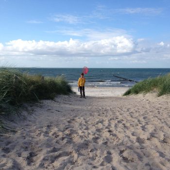 Ein Kind geht mit Fischer-Ausrüstung an den Ostsee-Strand