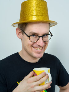 Person med guldfärgad hatt, glasögon och mumin mugg.