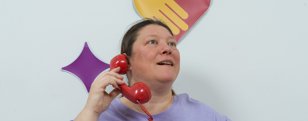 En person håller i en röd, gammeldags telefonlur, och pratar samtidigt med någon annan.
