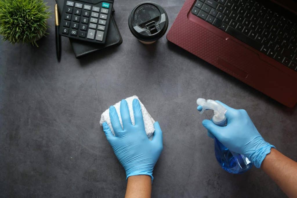 person sprayar rengöringsmedel på ett skrivbord med blåa gummihandskar