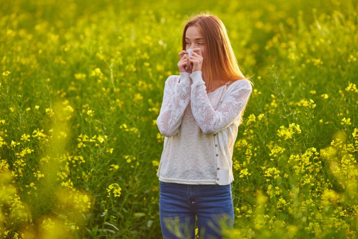 Pollen allergy, girl sneezing in a field of flowers