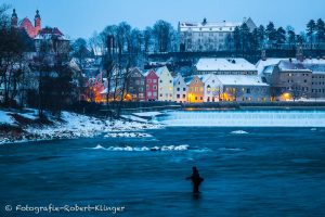 Ein Angler steht im eiskalten Lech vor dem Lechwehr und der Altstadt von Landsberg