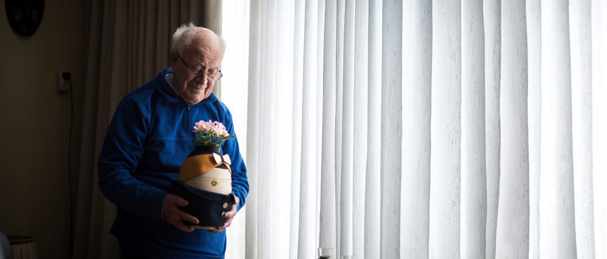 An older man holding the robot Tessa lovingly. He's standing in front of a window.