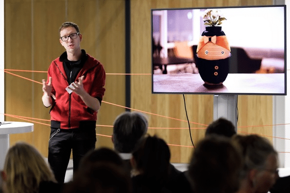 Photo of Robert A. Paauwe presenting at a conference. The robot Tessa is on screen behind him