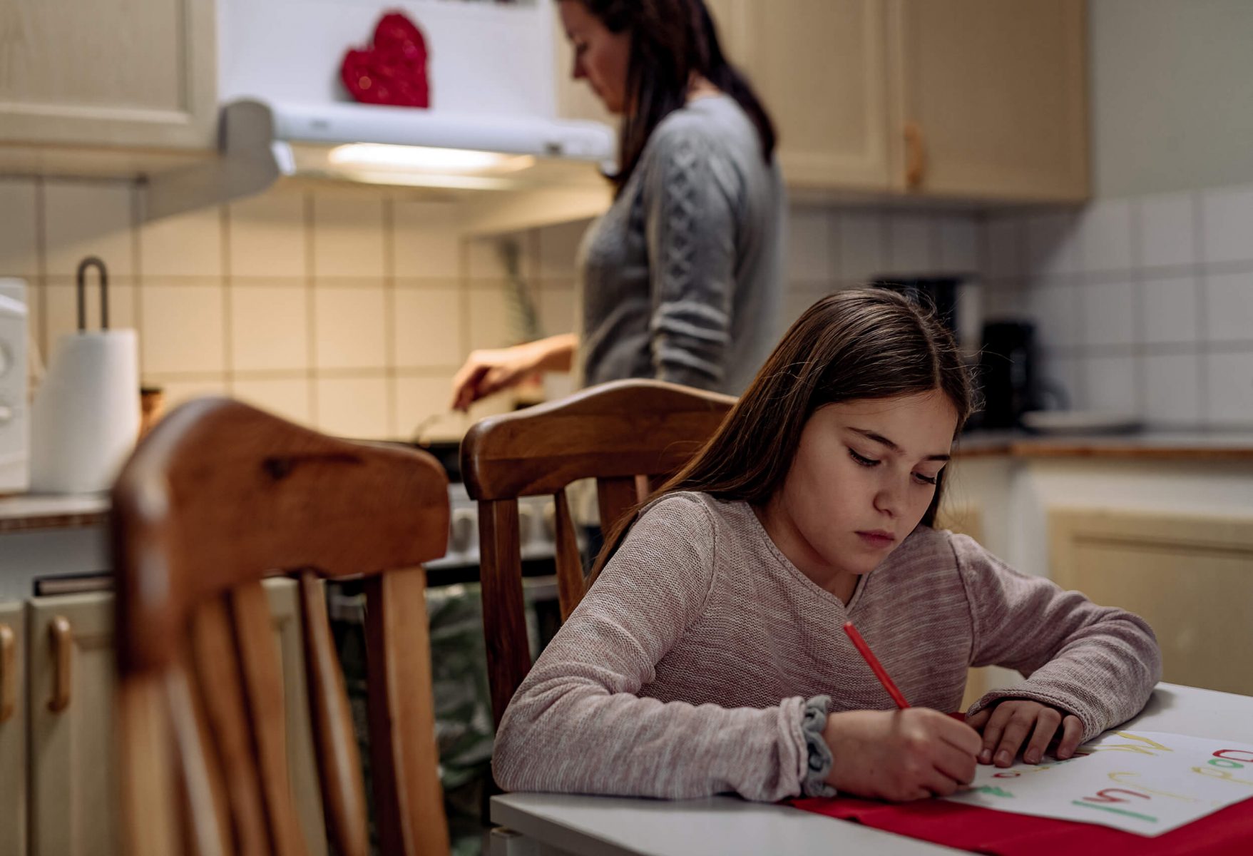 Kid making a Christmas card in kitchen. Looks bored and sad