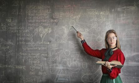 strict female teacher with book pointing at scribbled blackboard